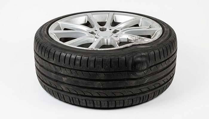 Low profile tire sidewall showing a pinch bulge from pothole impact next to an alloy wheel with a damaged rim edge