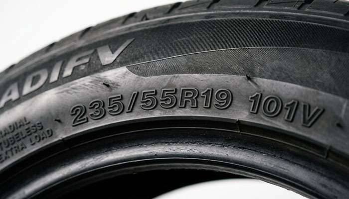 Close-up of a 235/55R19 tire sidewall showing the molded size designation, load index, and speed rating characters