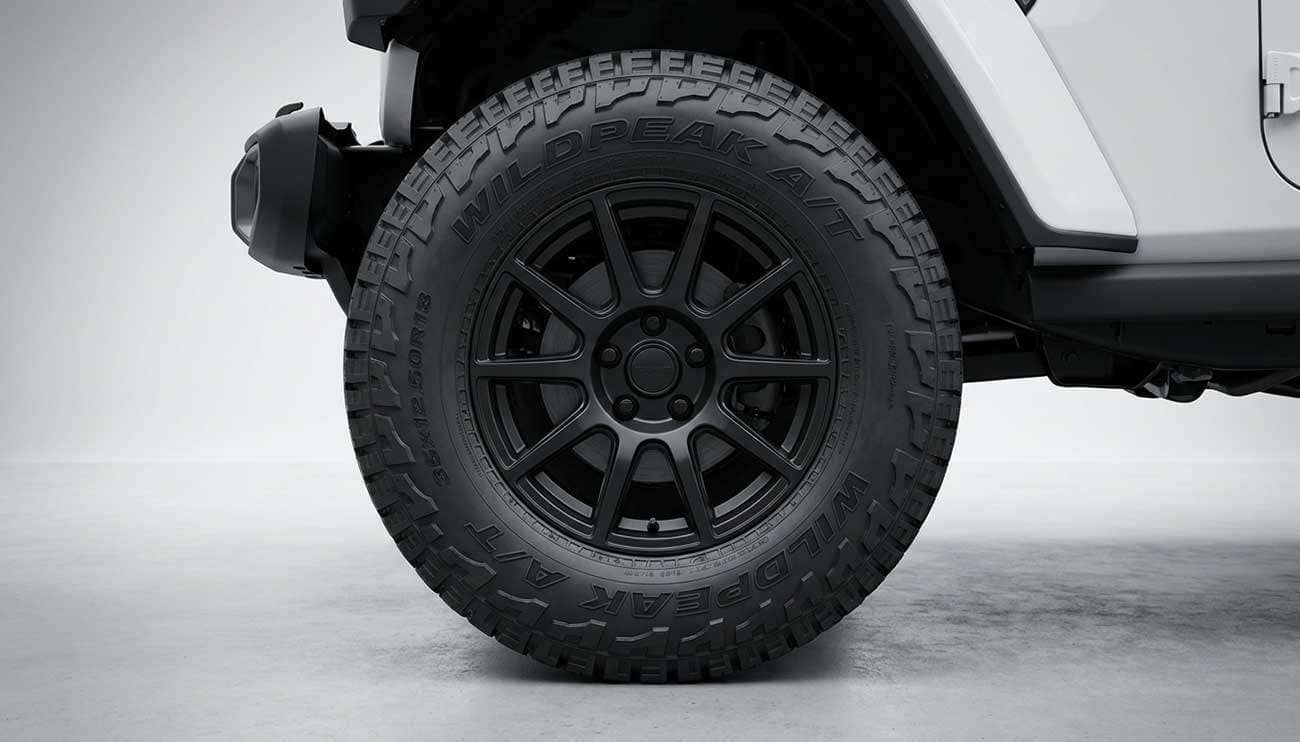 Close-up of a large off-road tire mounted on a black rim against a gray background on a white vehicle