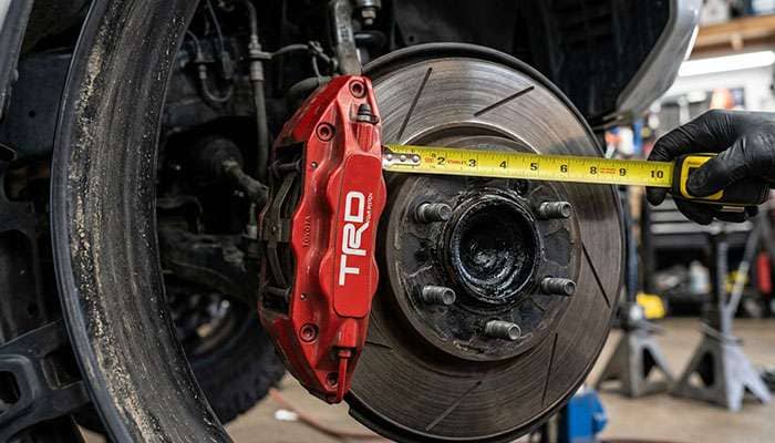 Large front brake caliper and rotor on a 4Runner hub with a tape measure checking clearance to a wheel barrel