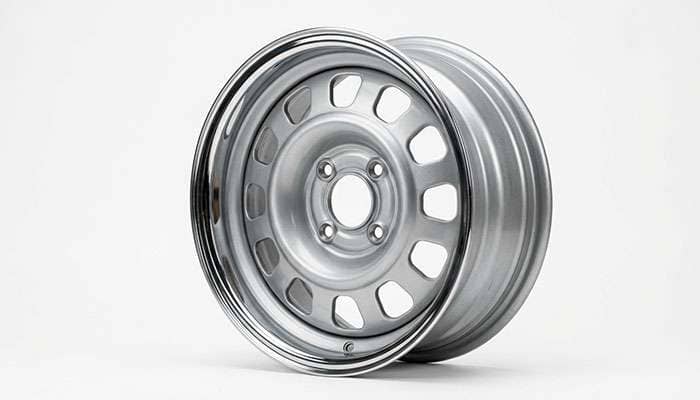 Four lug steel wheel from an early nineteen eighties American coupe shown against a plain background