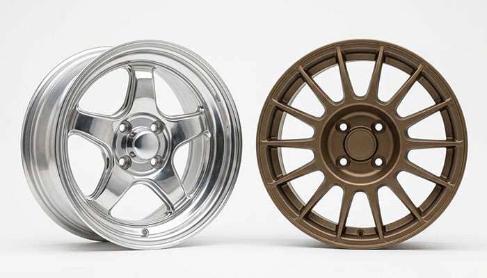 Two four lug wheel styles side by side, a vintage polished five spoke and a modern rally style wheel, on a clean white seamless backdrop