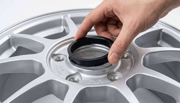 Black hub-centric ring being seated into the open center bore of an aftermarket alloy wheel before mounting