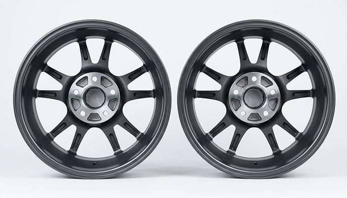 Two alloy wheels laid face down side by side showing a smaller 5x115 bolt circle next to a larger 5x127 bolt circle