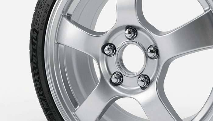 Close-up of a 5x4.5 bolt pattern on a silver car wheel with five lug nuts and a black tire