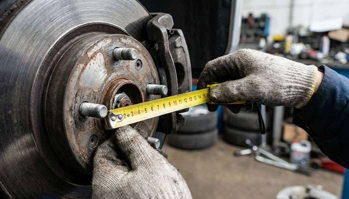 Hands measuring the distance between wheel bolts on a car hub with a yellow tape measure