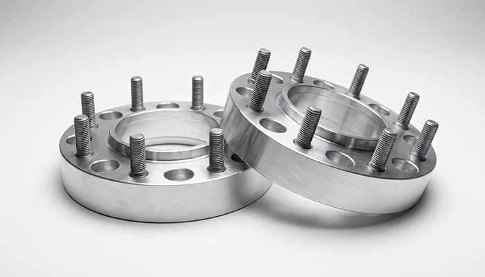 Pair of silver aluminum wheel spacers with bolts and a small red and white tube of lubricant below them