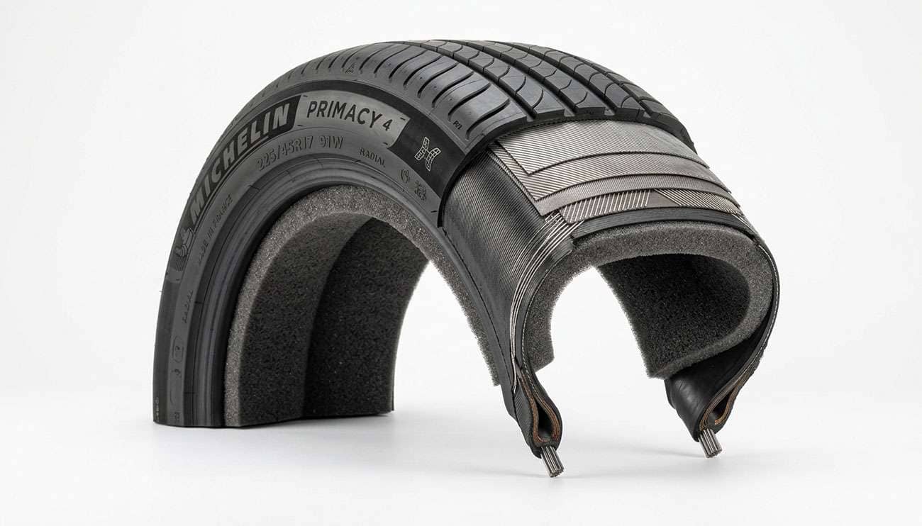 Cutaway passenger tire revealing a black acoustic foam layer bonded to the inner liner, studio product photo