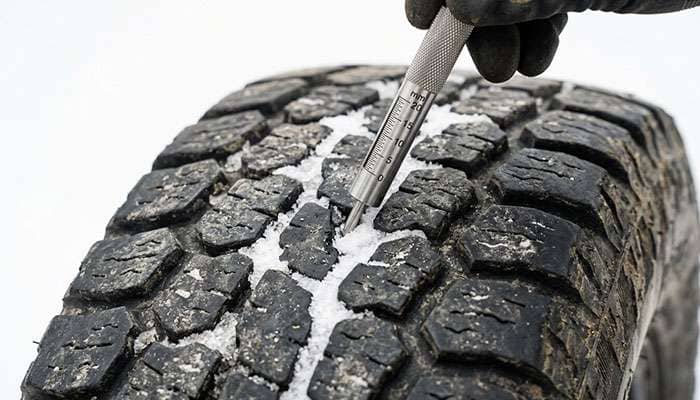 Tread depth gauge measuring the remaining tread on a worn all-terrain tire with packed snow in the grooves