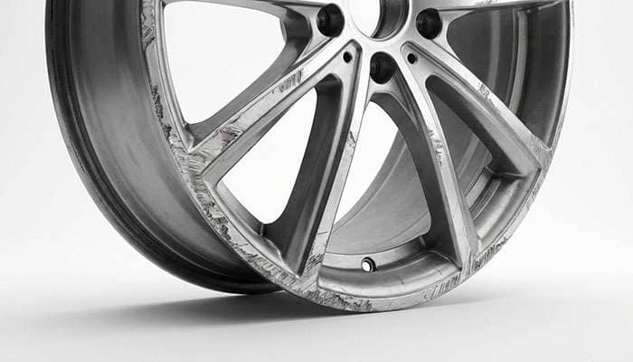 Close-up of an alloy wheel with visible curb rash damage and a logo for alloy wheel repair specialists