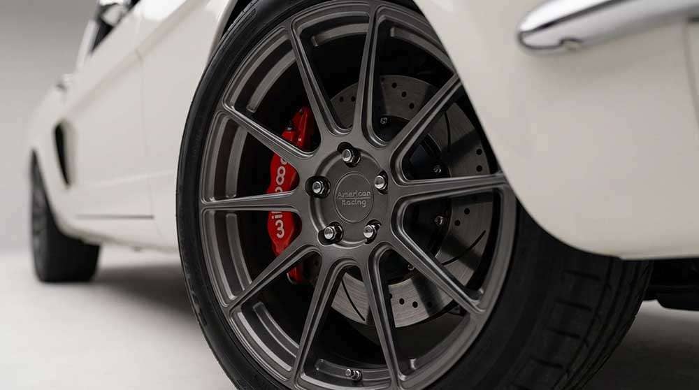 Close-up of the gray American Racing VF510 wheel and red Wilwood brake caliper on a 1965 white Ford Mustang Shelby