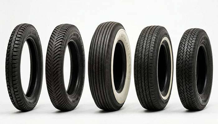 Five antique car tires from different brands standing upright on a clean white studio surface showing variety of whitewall and blackwall options