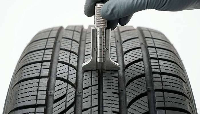 Tread depth gauge measuring an all-season crossover tire before matching AWD tires
