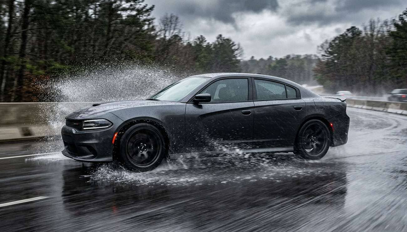 Modern sports sedan driving on rain-slicked road with water spray off tires