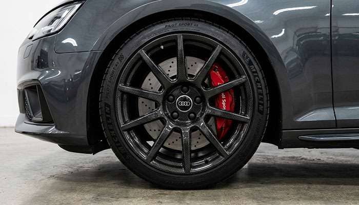 Close-up of a sleek black carbon fiber car wheel and tire on a dark gray vehicle against a plain background