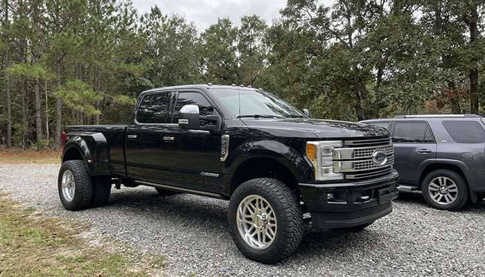 Black dually truck with chrome wheels and Falken tires parked outdoors near trees and another vehicle