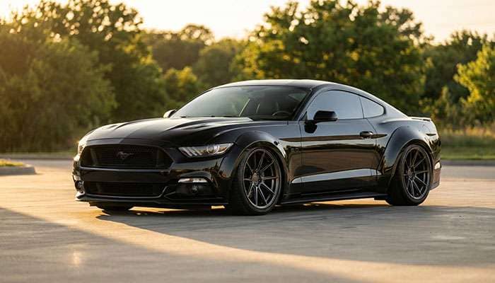 Sleek black S550 Mustang with aggressive wheel fitment and lowered stance parked on a concrete surface with trees in background
