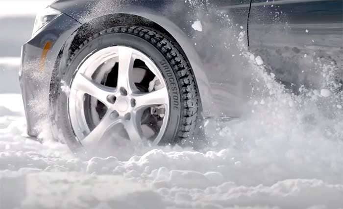Close-up of a car tire splashing through snow, showcasing the Bridgestone Blizzak WS90 winter tire tread