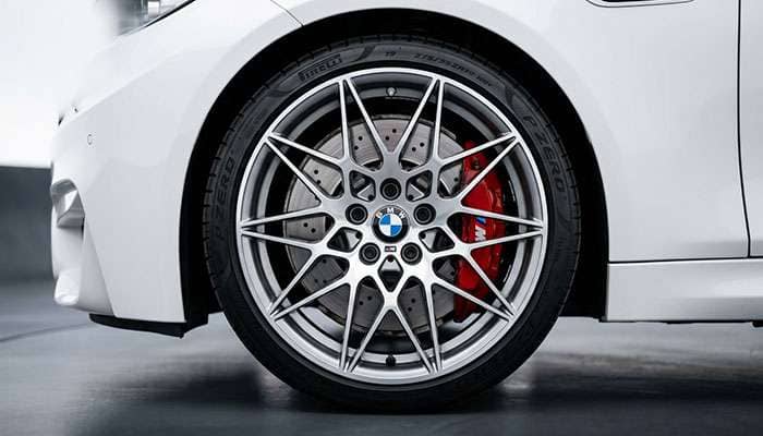 Close-up of a sporty BMW car wheel with a multi-spoke alloy rim and red brake caliper on a white vehicle.