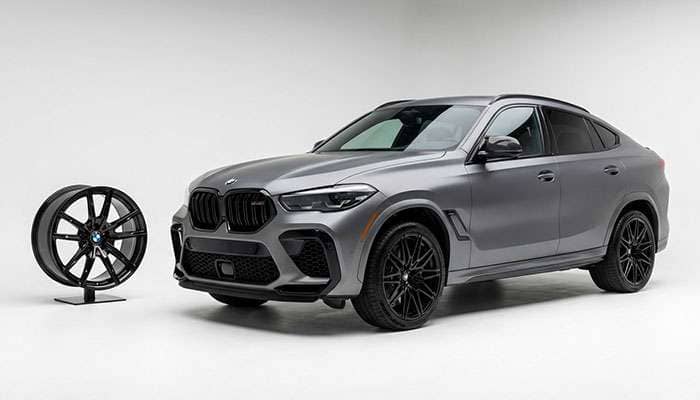 Matte gray BMW X6M F96 LCI with black forged wheels by Larte Design next to a large display wheel
