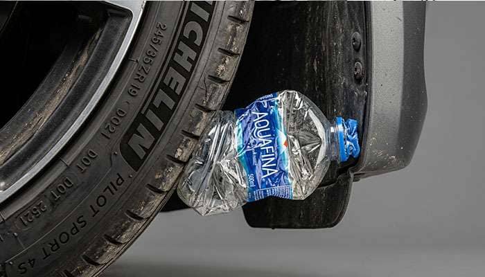 Close-up of empty plastic water bottle pressed between car tire and fender wheel well