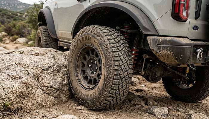Rear wheel of a Ford Bronco on a 35-inch tire under a high-clearance fender flare with the suspension compressed on a rock