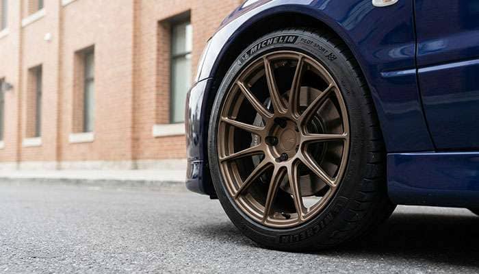 Close-up of bronze aftermarket wheels and tires on a blue Mitsubishi Lancer EVO 8 or 9 parked on a street.