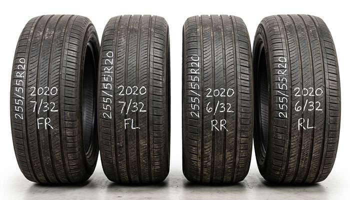 Four used tires for 2020 Buick Enclave with size markings written in white chalk, displayed vertically indoors.