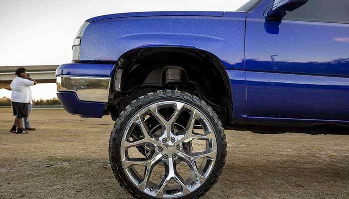 Bright blue Carolina squat truck with oversized front wheels lifted higher than rear wheels on a grassy field