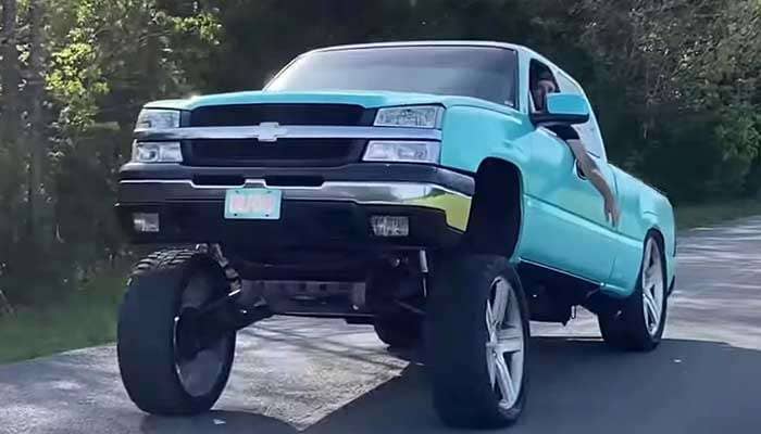 Light blue lifted pickup truck with extreme front suspension lift known as the Carolina squat on a rural road