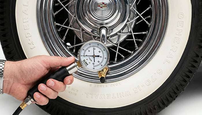 Checking tire pressure with a gauge on a classic car tire