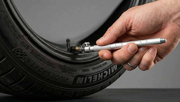 Hand using a tire pressure gauge on a tire valve stem to check PSI before long-term storage