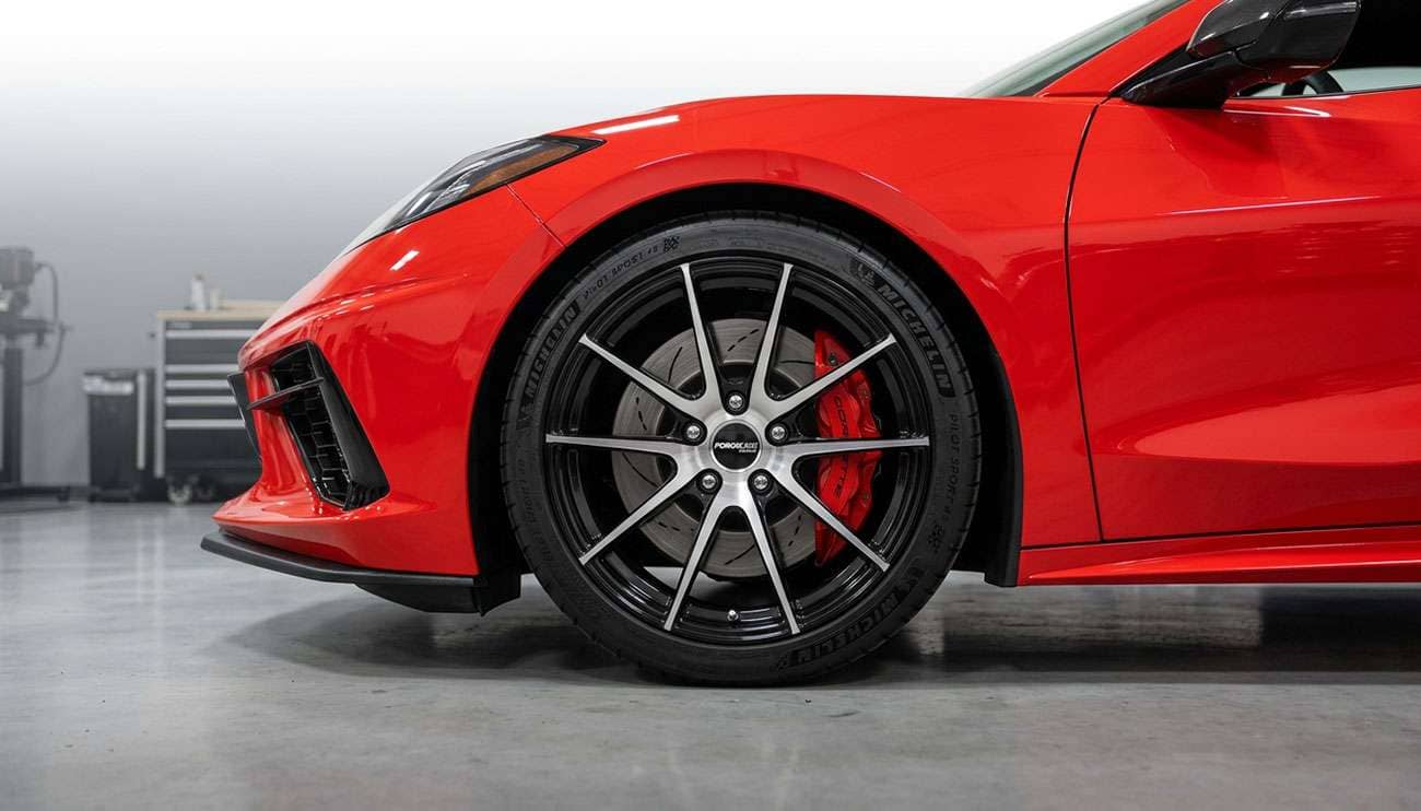 Close-up of a red Chevrolet Corvette showcasing sleek aftermarket wheels in a garage setting.