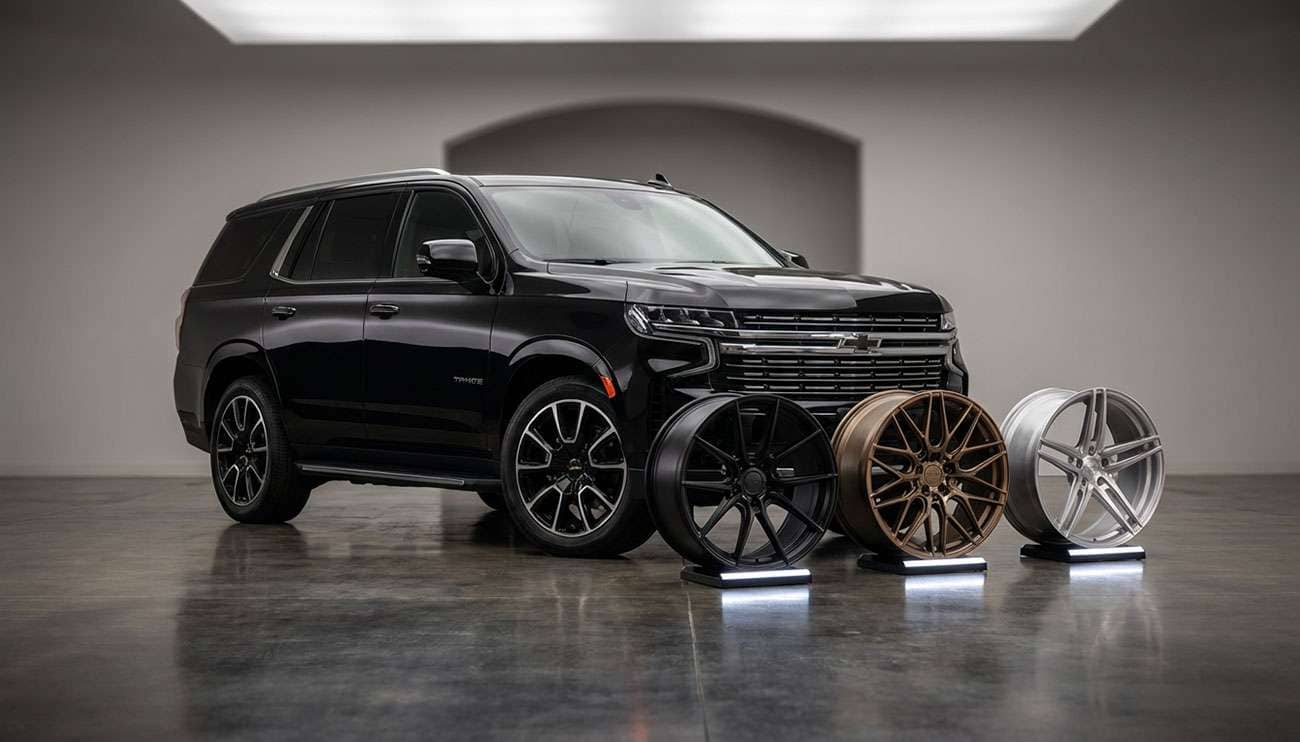 Black Chevrolet Tahoe parked indoors with three distinct aftermarket wheel options displayed in front