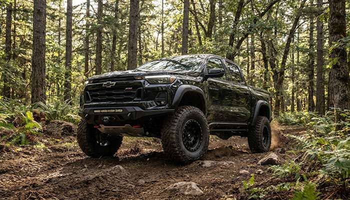 Black 2024 Chevrolet Colorado with super aggressive 3-5 inch wheel offset and large off-road tires in forest setting