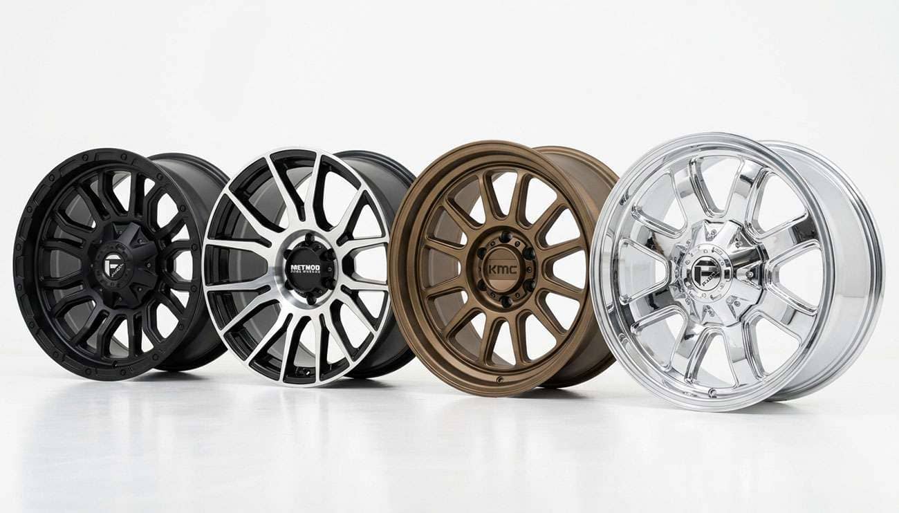 Row of aftermarket pickup truck rims in various finishes lined up on a clean white studio backdrop