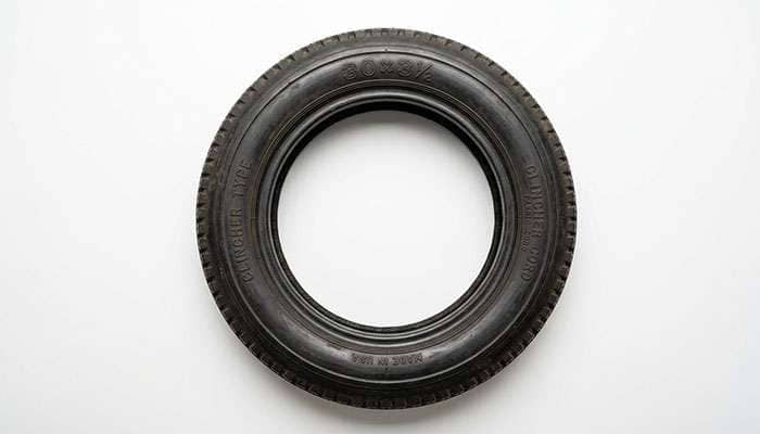 Close-up of a brass era clincher tire sidewall showing vintage high-pressure sizing numbers on a clean white surface