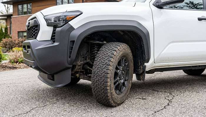 Front tire of a midsize pickup at full steering lock showing clearance to the bumper cover and fender liner
