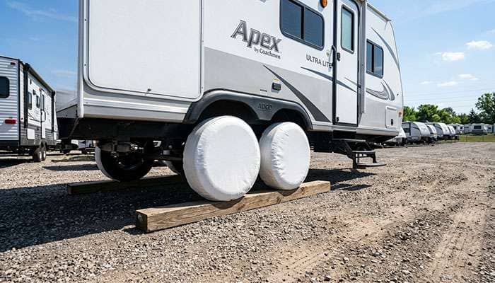 Tandem axle travel trailer in storage with white vinyl covers over the tires to block sunlight