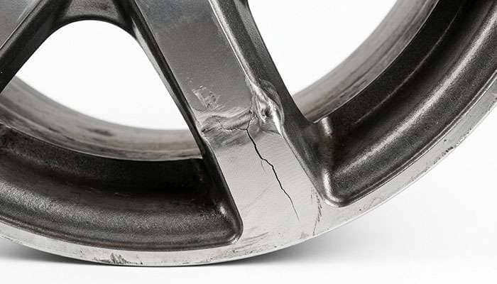 cast aluminum wheel showing a hairline crack radiating from a previously straightened bend near the spoke junction