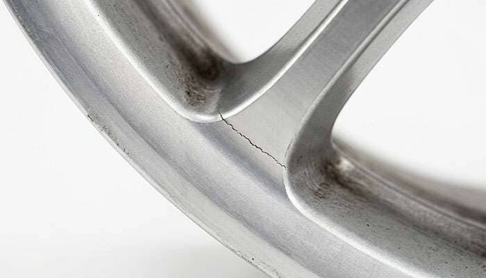 Close-up of a hairline crack forming at the spoke to barrel junction on an overloaded aluminum wheel