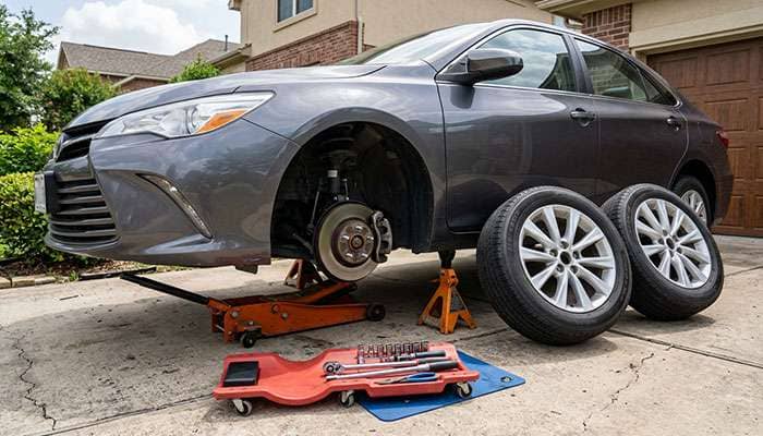 Two front wheels removed and set beside a car on jack stands in a driveway for a left to right tire swap test