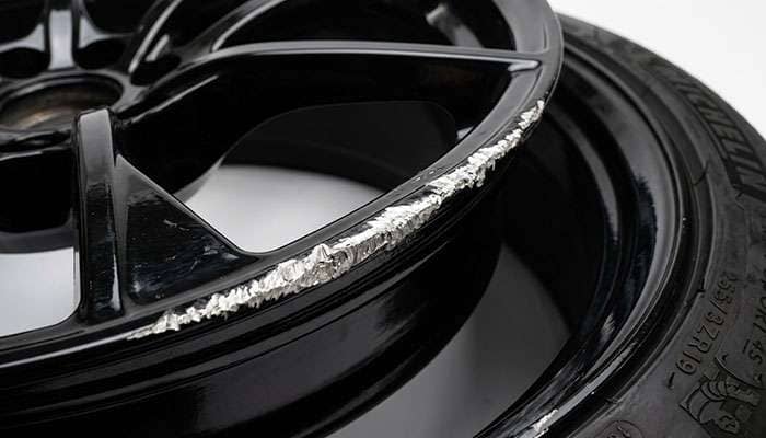 Curb rash damage on the lip of a gloss black alloy wheel exposing bright metal
