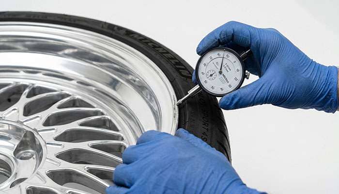 Machinist inspecting curb damage on the polished lip of a forged aluminum wheel before repair