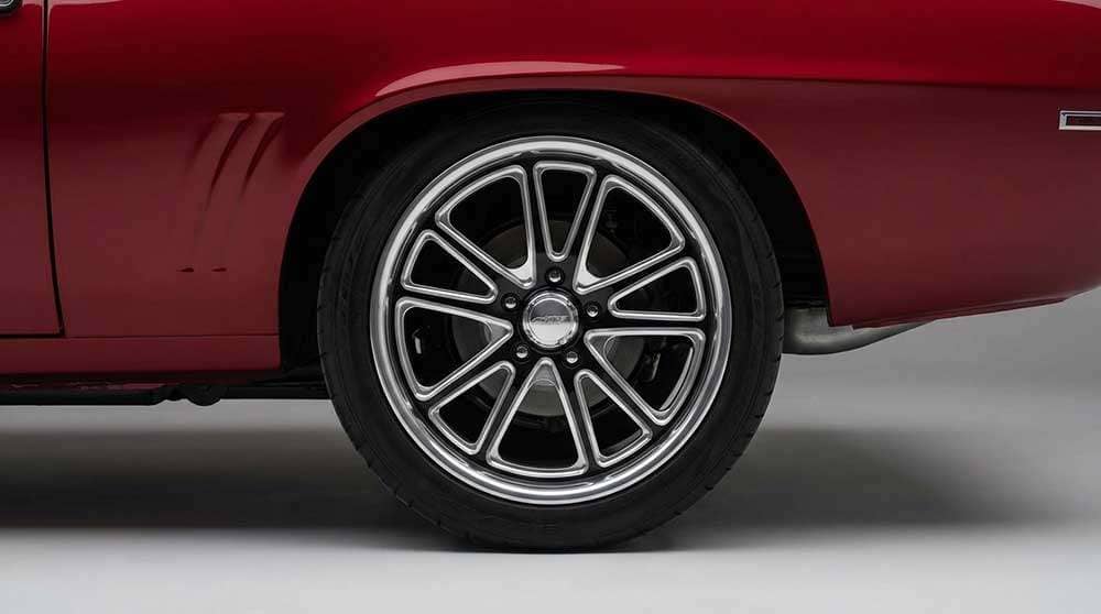Close-up of a custom billet wheel with polished spokes and black accents on a red muscle car
