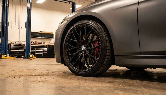 Close-up of a sleek matte gray car featuring custom black powder-coated alloy wheels in a garage setting