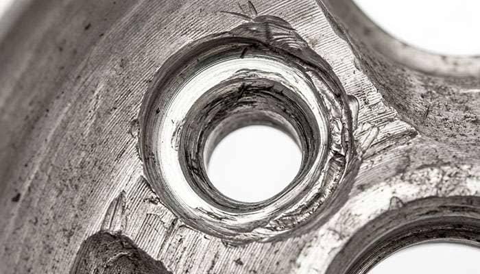 Close-up of an aluminum wheel lug hole with a deformed and elongated seat from incorrect lug nuts