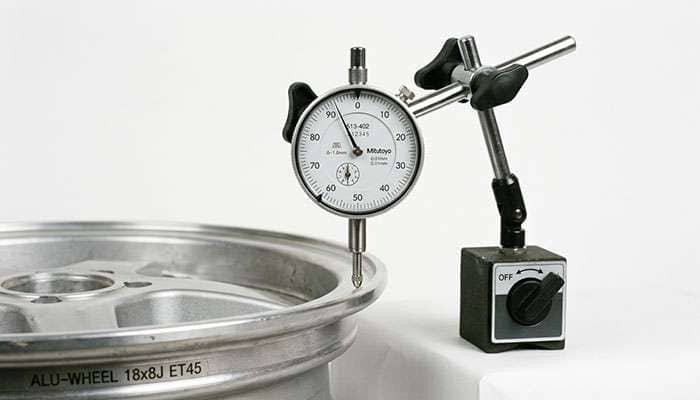 dial indicator gauge positioned against the flange of a wheel to measure lateral runout in thousandths of an inch