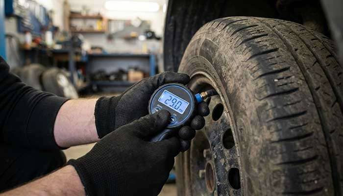 Person wearing gloves using a digital tire pressure gage to check car tire pressure at 29.0 psi