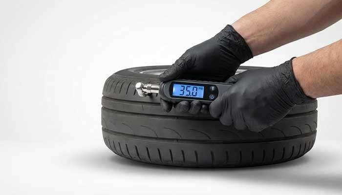 Person wearing gloves using a digital tire pressure gage to check a car tire's pressure reading of 29.0 psi.